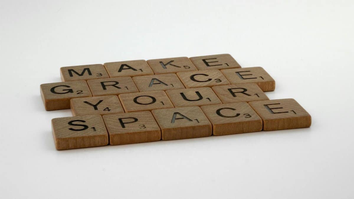 Wooden Scrabble tiles form the message "Make Grace Your Space" on a white surface.