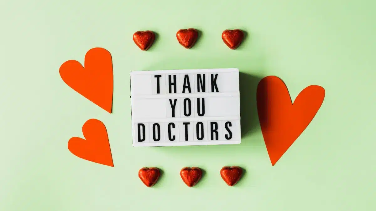 Top view of red heart shaped decorative elements and white retro light box with THANK YOU DOCTORS gratitude message arranged on green background
