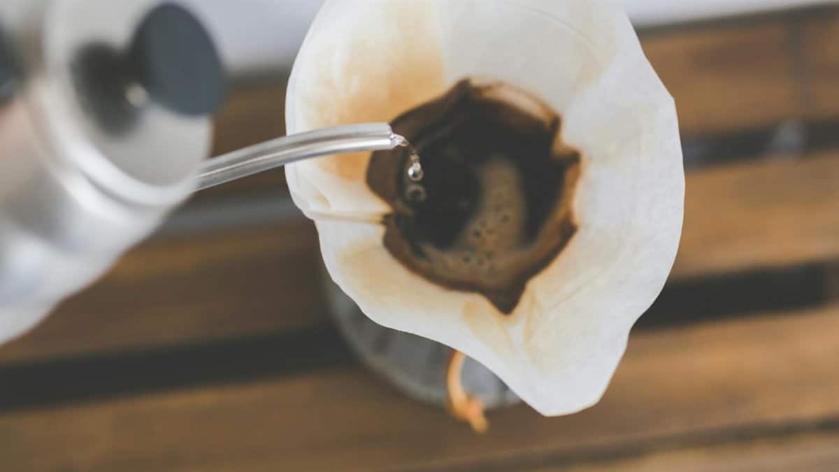 Close-up of pour over coffee brewing with filter paper and kettle pouring hot water.