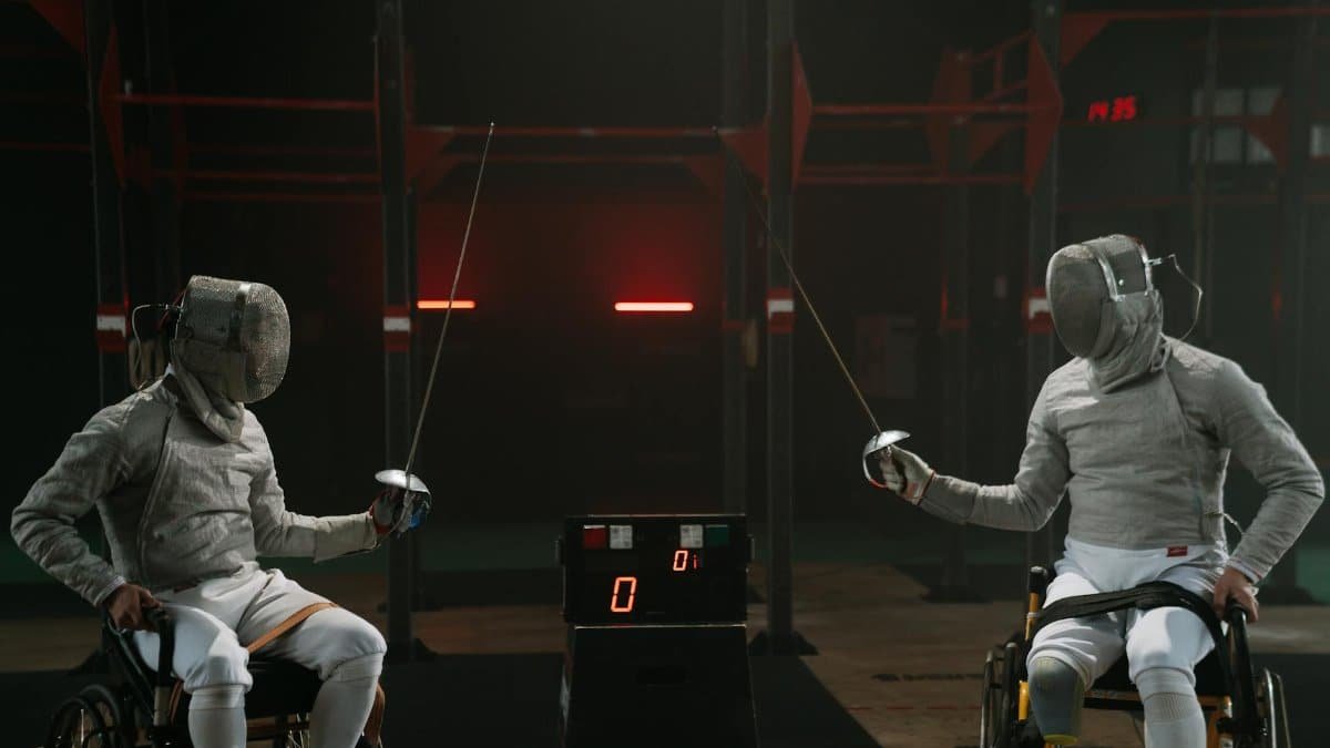 Two male wheelchair fencers in an intense match indoors, showcasing skill and determination.