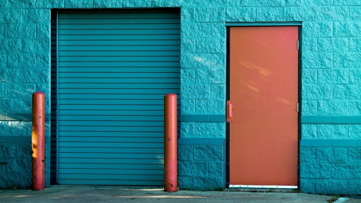 Vivid blue wall with a closed door and shutter in Valparaiso's urban setting.