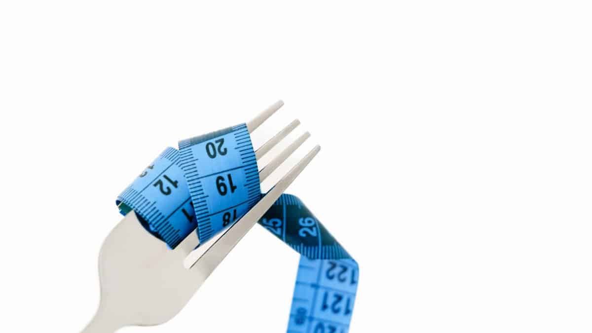 A fork wrapped with a blue measuring tape symbolizing diet and weight management.