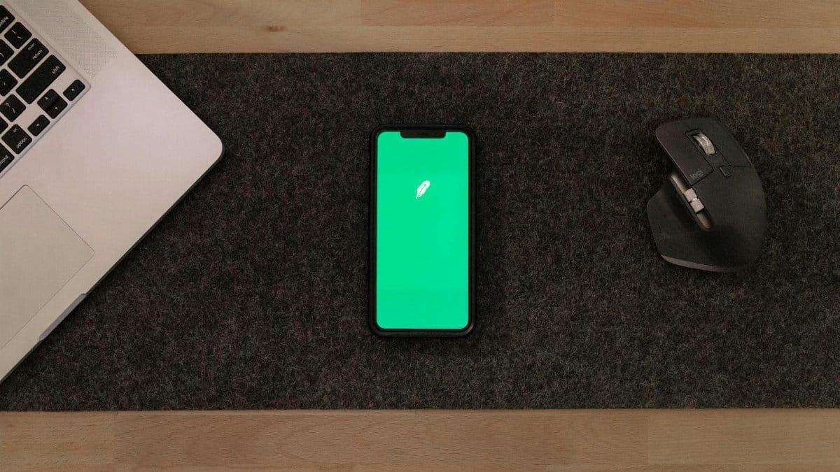 Modern workspace with smartphone, laptop, and mouse on wooden desk.