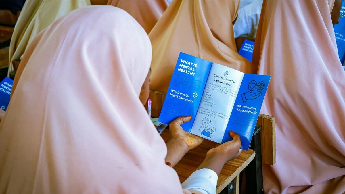 Women in classroom exploring mental health pamphlet, educating in Kaduna, Nigeria.
