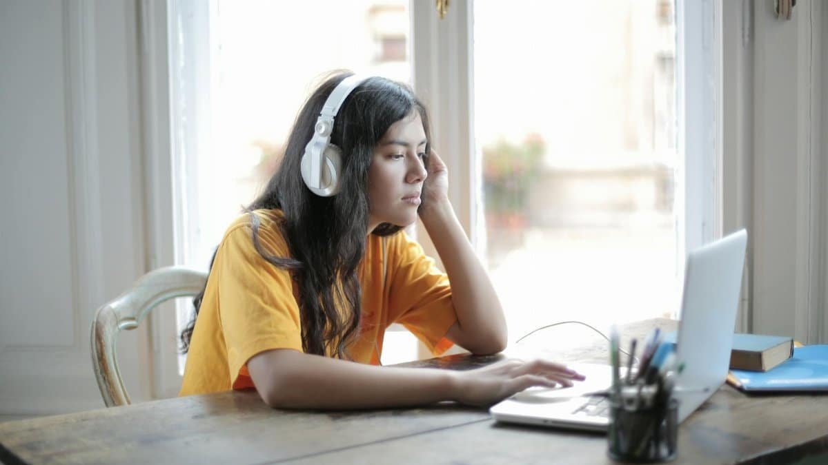 Focused woman in yellow shirt using a laptop while listening to music indoors.