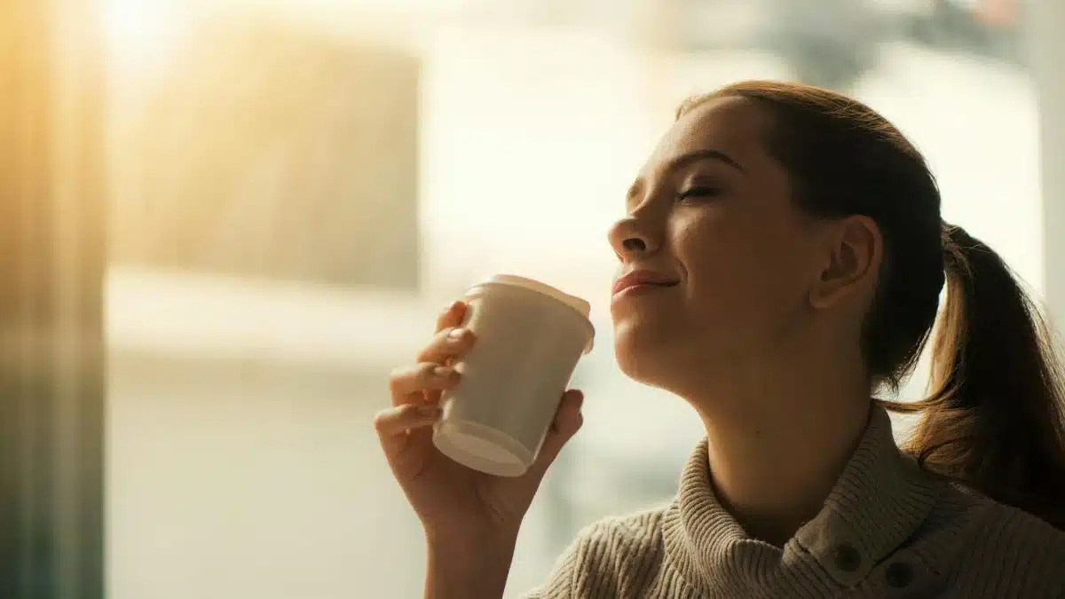 Smiling woman savoring morning coffee by the window in soft warm light.
