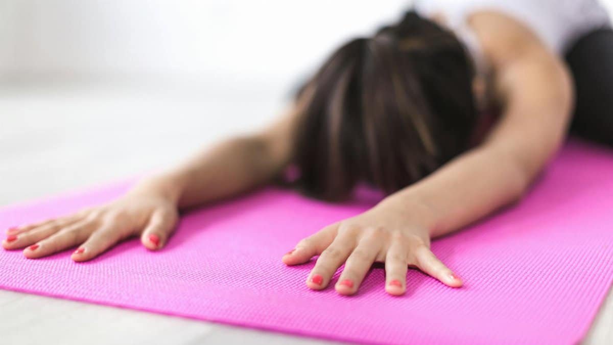 Close-up of woman stretching on a pink yoga mat, promoting relaxation and mindfulness.