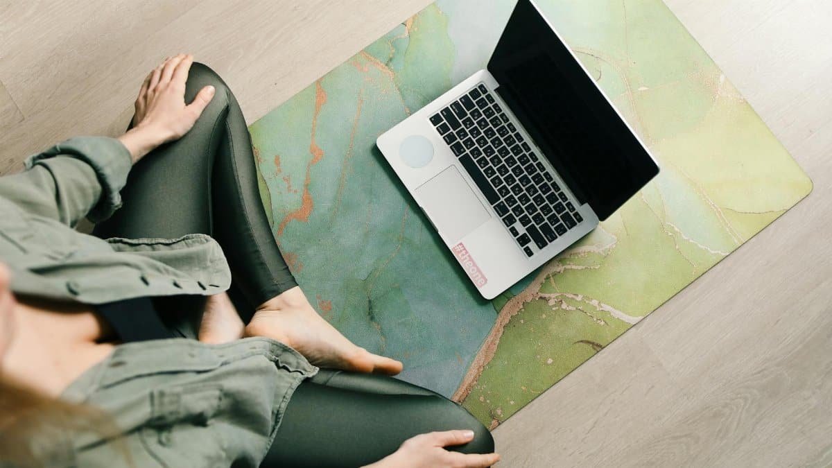 A woman meditates on a yoga mat with a laptop, blending wellness and technology.