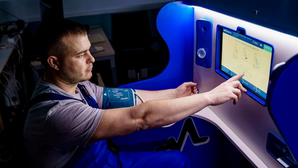 A man uses a touch screen for a telemedicine health check in a modern setting.