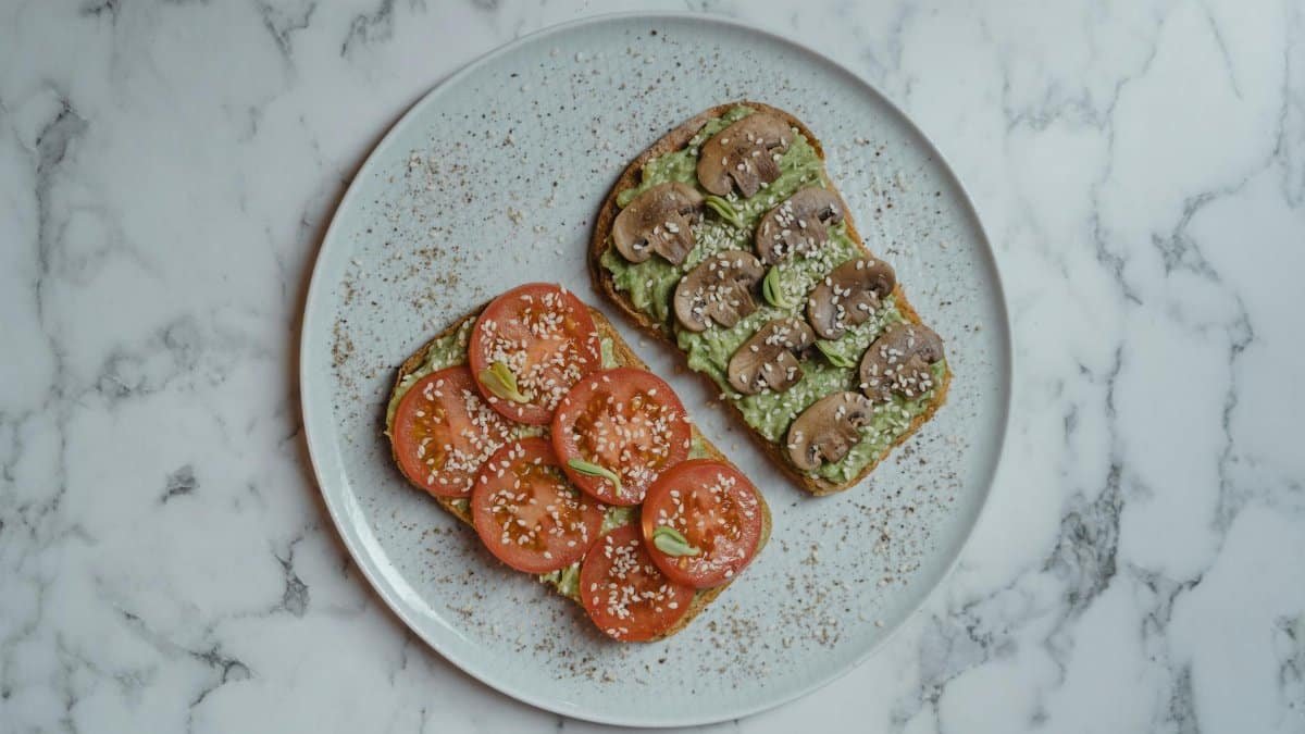 Healthy vegan avocado toast with tomatoes and mushrooms on a marble background.