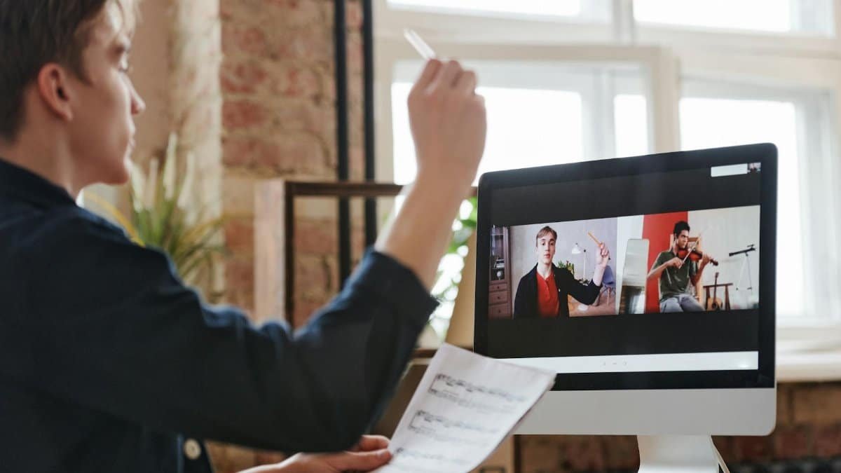 A man participates in a virtual music lesson, interacting with a violin teacher via video call.