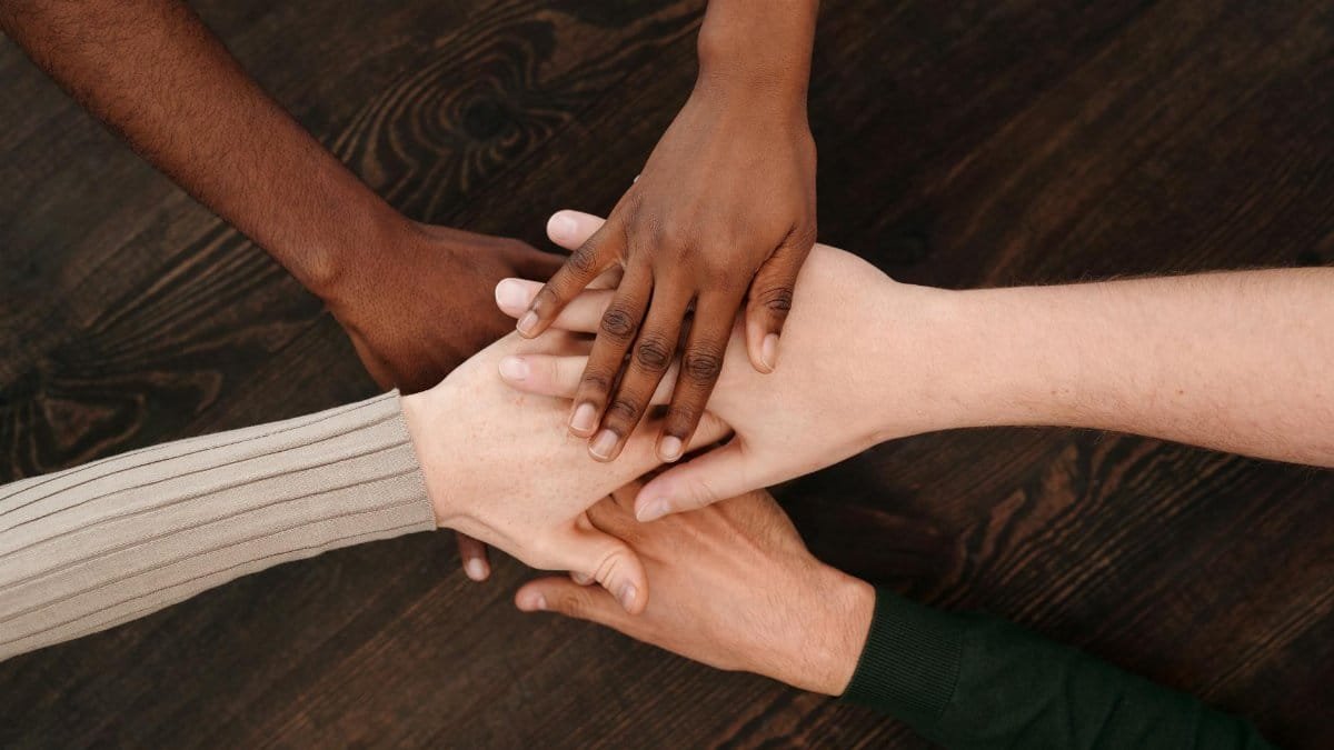 A diverse group of hands joining together, symbolizing unity and teamwork on a wooden surface.