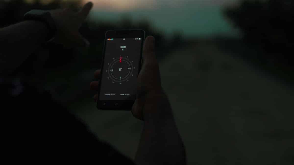 Person navigating using a smartphone compass app outdoors at twilight.