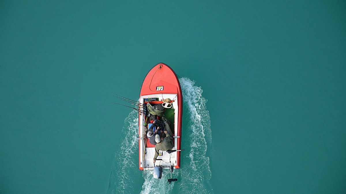 Top view of a red motorboat with fishermen navigating open turquoise waters.
