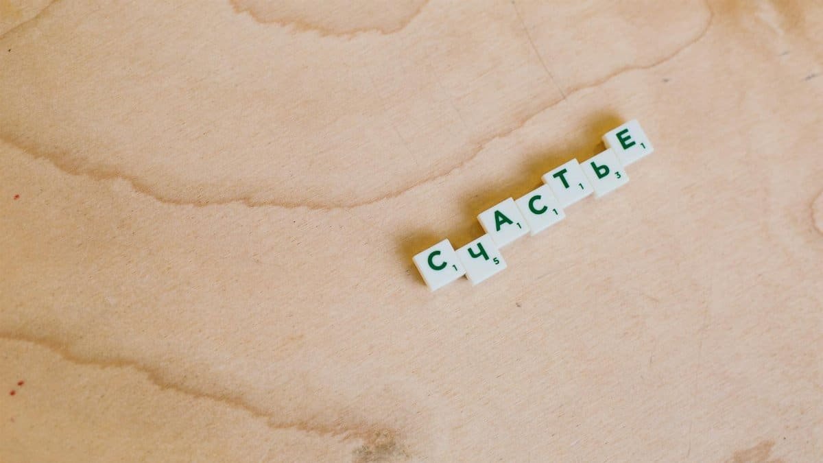 Cyrillic Scrabble tiles spelling 'happiness' on a wooden board.