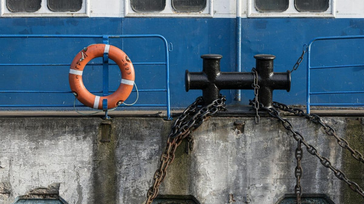 Close-up of a lifebuoy and anchor chains on a ship's deck, blue and white exterior.