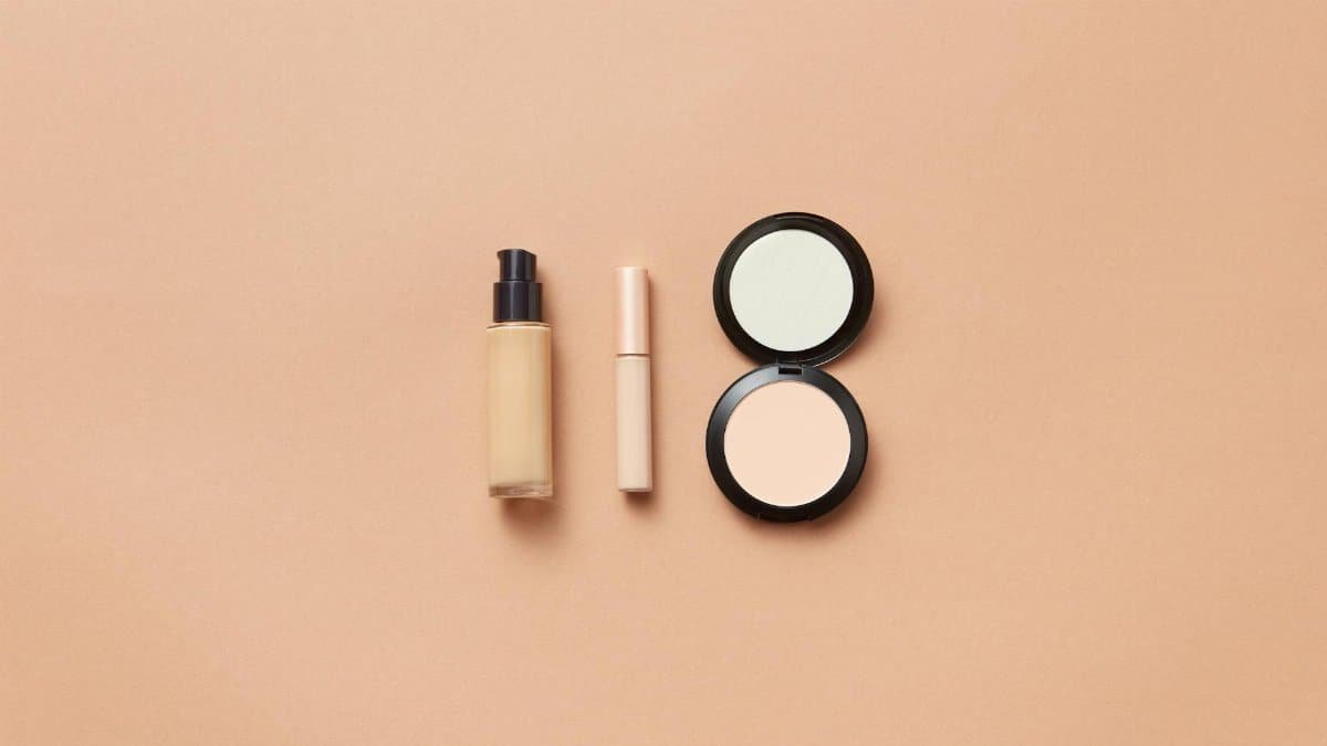 Flatlay of foundation, concealer, and compact powder on beige background. Perfect for beauty and cosmetic themes.