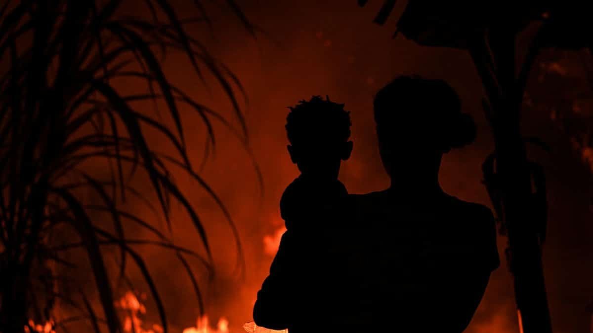Silhouette of a parent and child standing against a backdrop of a raging fire at night.