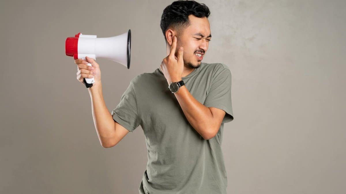 A man with a megaphone holding ear in discomfort, representing noise pollution or loud sounds.