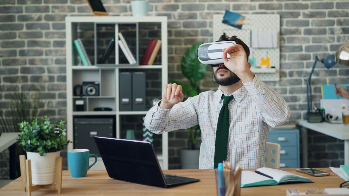 Man wearing VR headset explores virtual reality at desk in modern office setting.