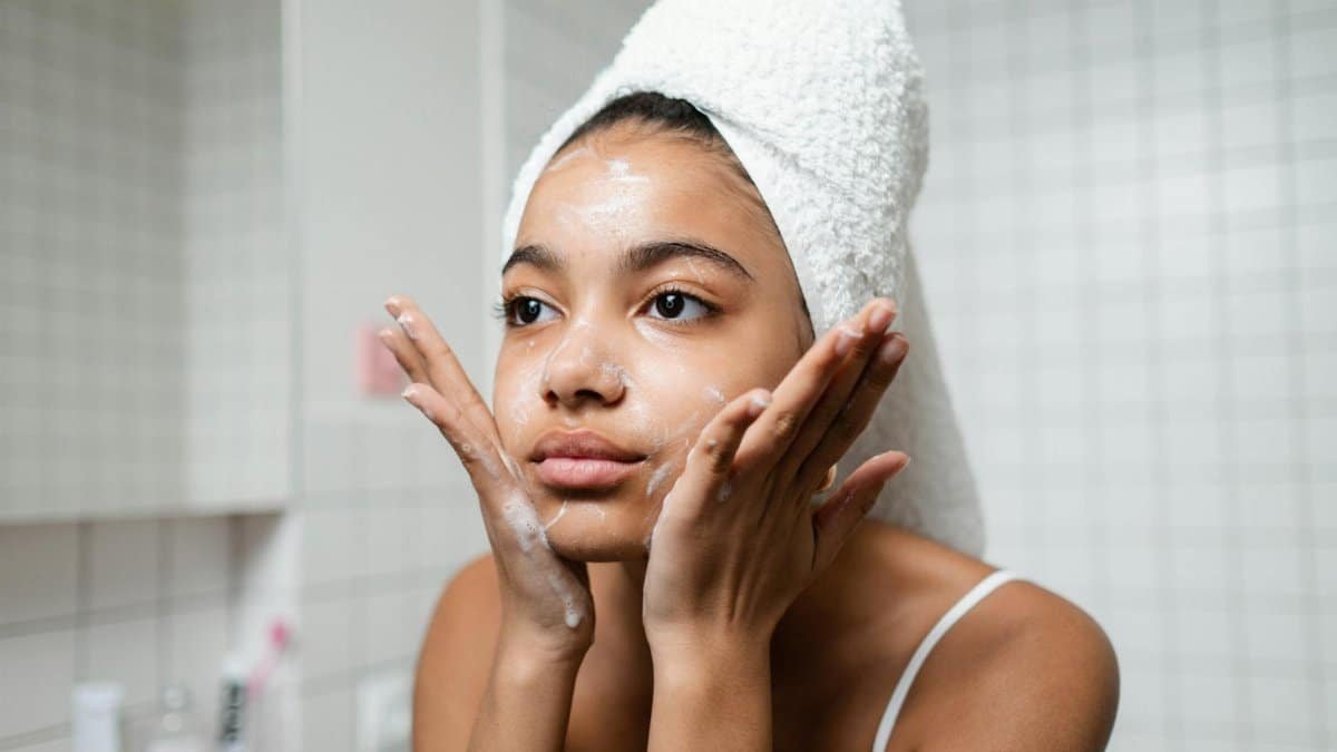 Young woman practicing skincare routine with a towel wrap indoors.