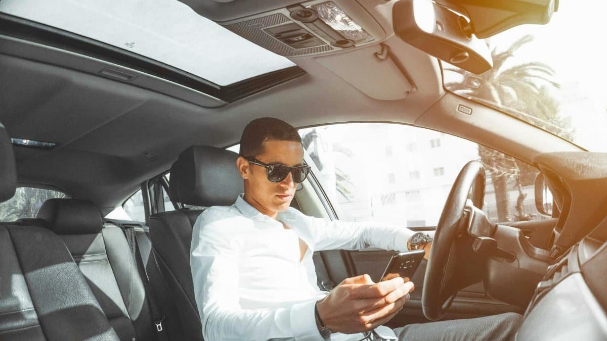 A man wearing sunglasses texts on his phone while driving a car in Morocco.