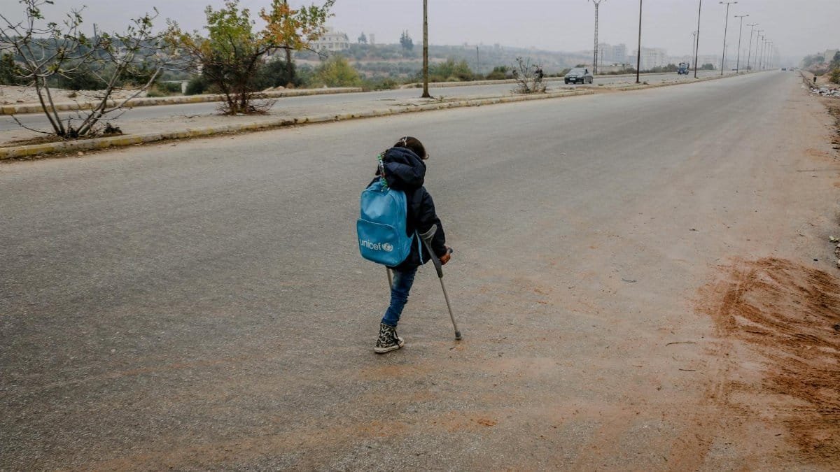 A young child with a crutch walking on a rural road in Idlib, Syria, symbolizing resilience.