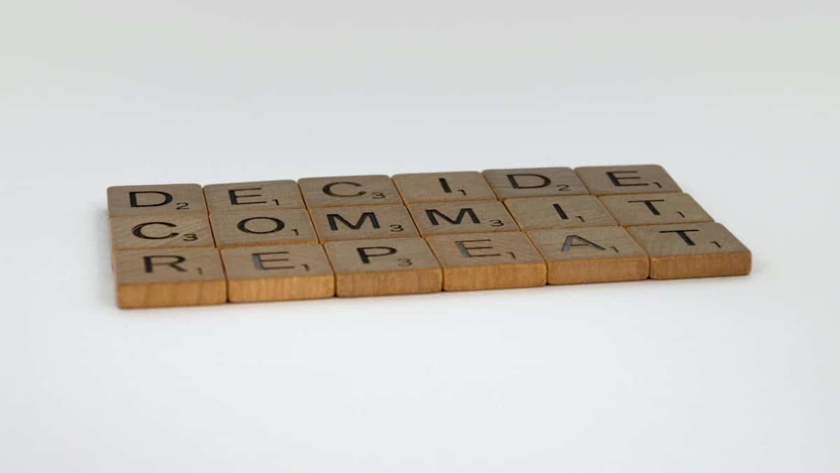 Wooden tiles arranged to spell 'DECIDE COMMIT REPEAT' on a white background.