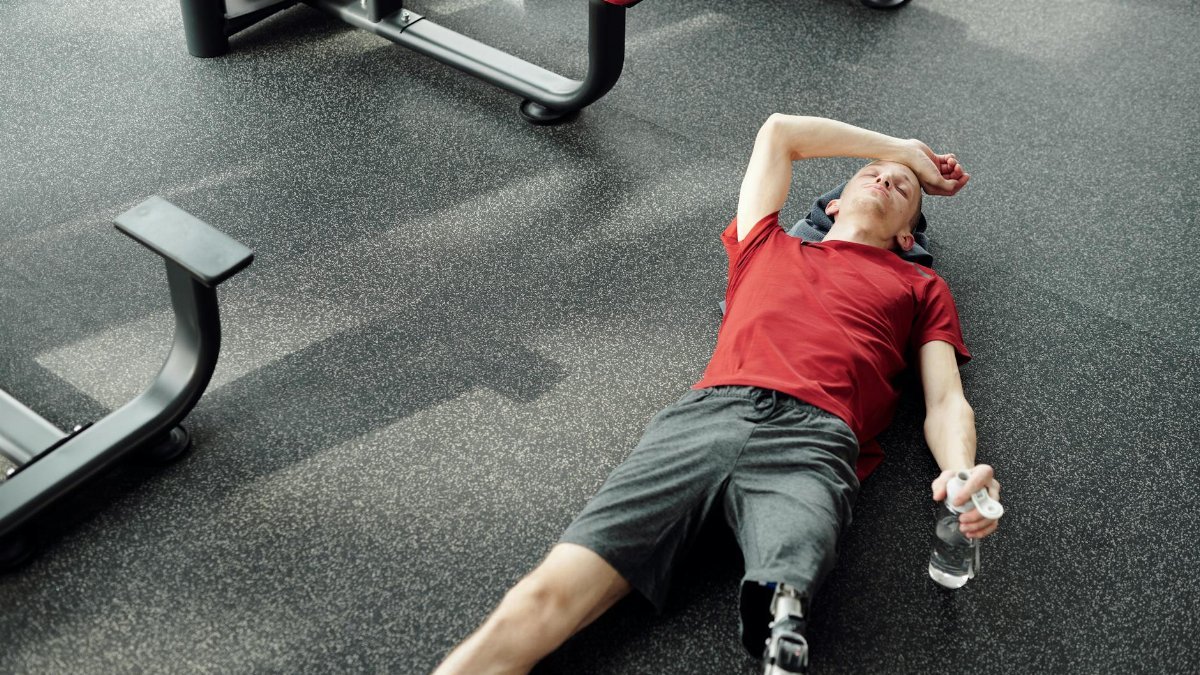 A man with a prosthetic leg rests on the gym floor, holding a water bottle after an intense workout.