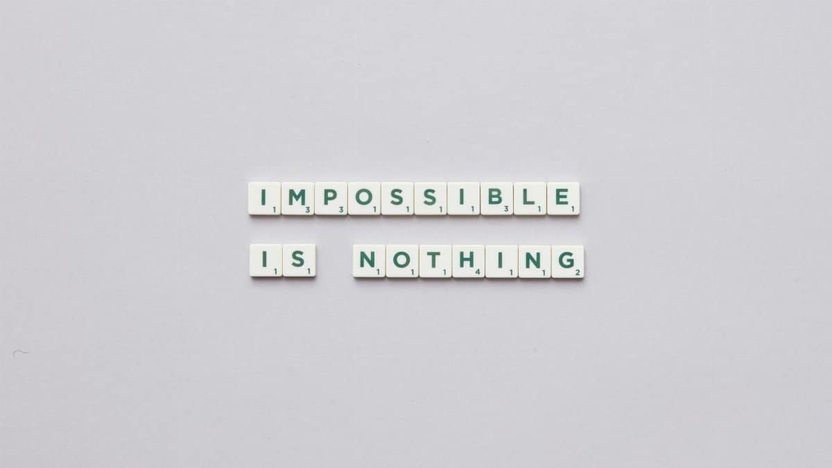 Flat lay of Scrabble tiles spelling 'Impossible is Nothing' on a neutral background.