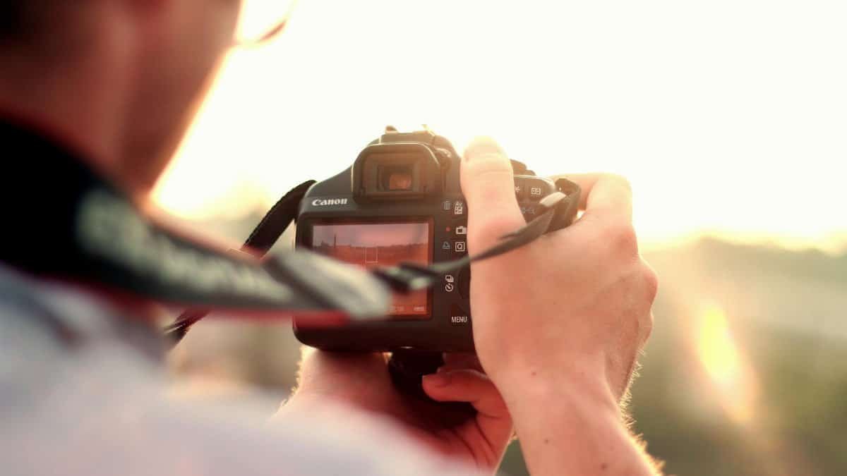 Photographer capturing a scenic outdoor view, holding a DSLR camera during sunset.