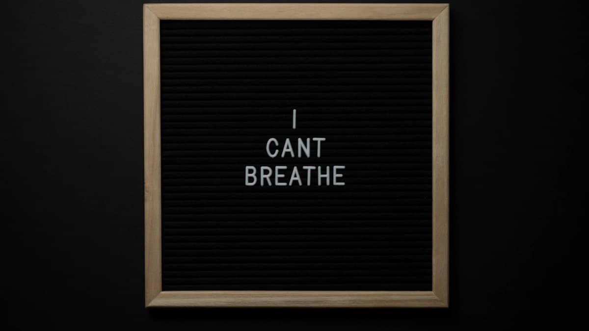 Top view of phrase I Cant Breath on small black signboard with light beige thin frame on black background
