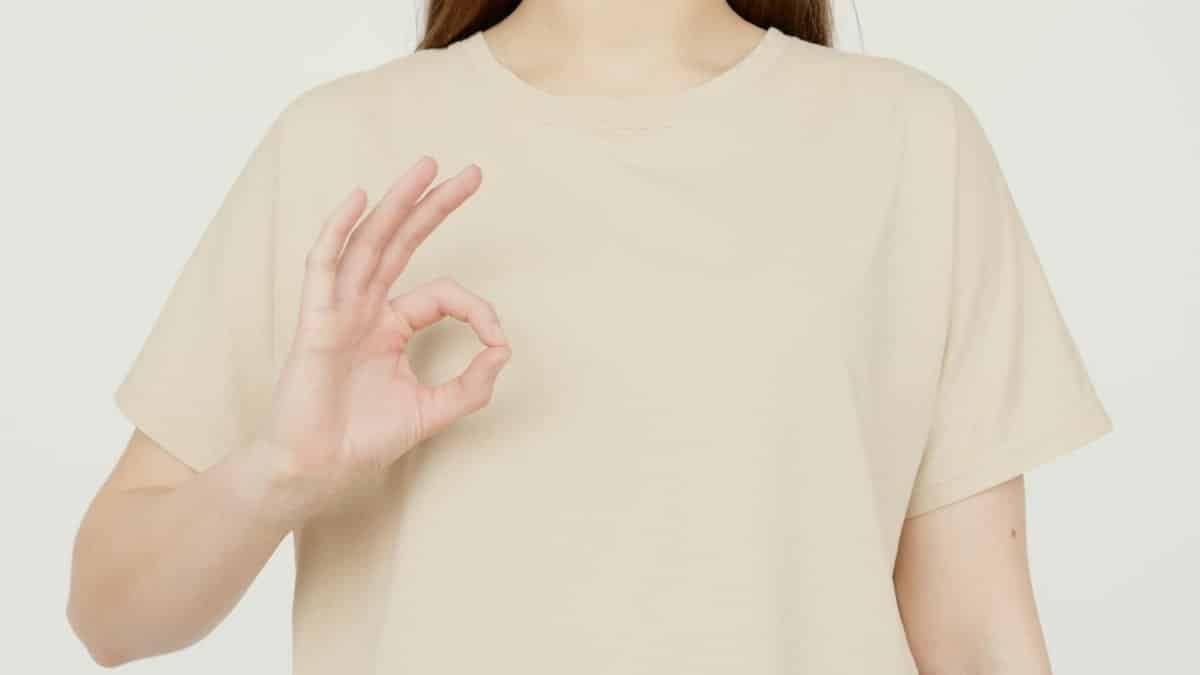 Close-up of a woman in a beige t-shirt making an okay gesture with her hand. Perfect for concepts of approval, satisfaction, and positivity.