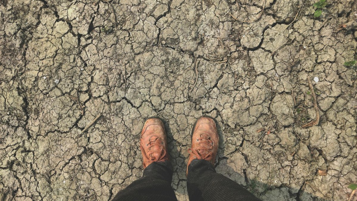 Brown shoes on dry, cracked soil signify drought conditions and environmental concerns.