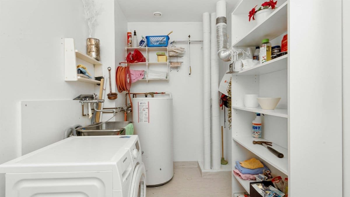 Clean and organized home laundry room with washing machine, shelves, and water heater.