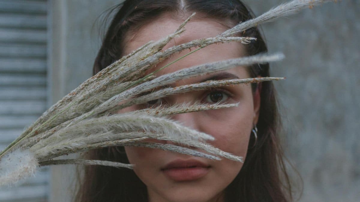 Artistic portrait of a woman with grass stalks obscuring her face, creating a mysterious and serene mood.