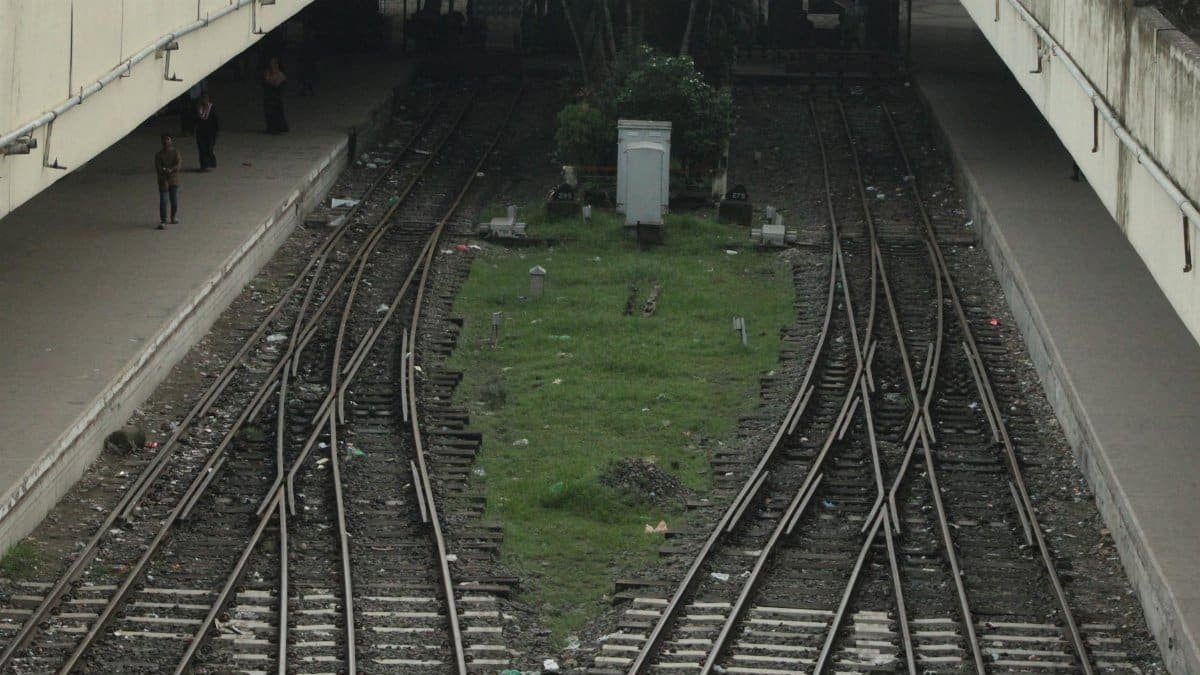 Converging train tracks in an urban station with platforms and people.
