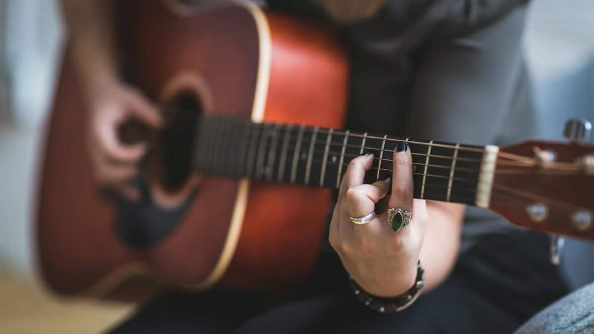 Detailed shot of a woman's hands playing an acoustic guitar indoors.