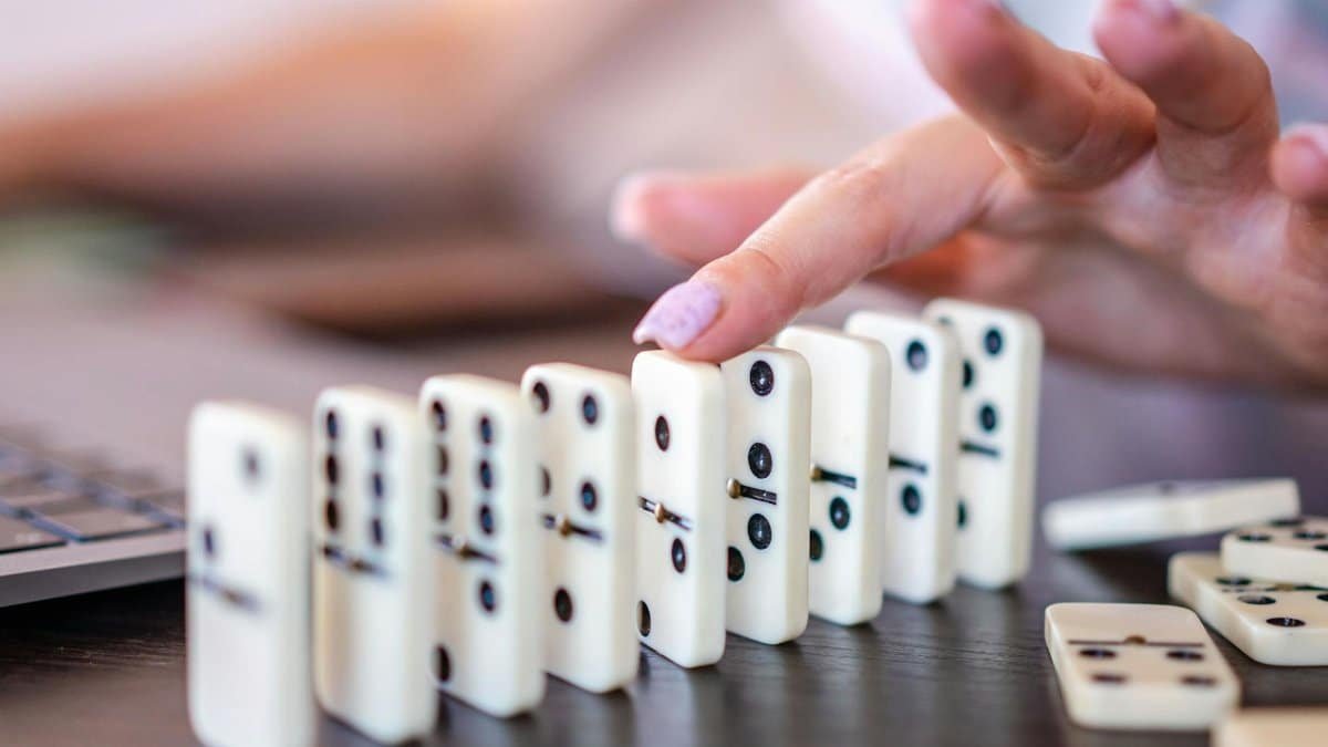 Fingers delicately push domino tiles, causing a chain reaction.