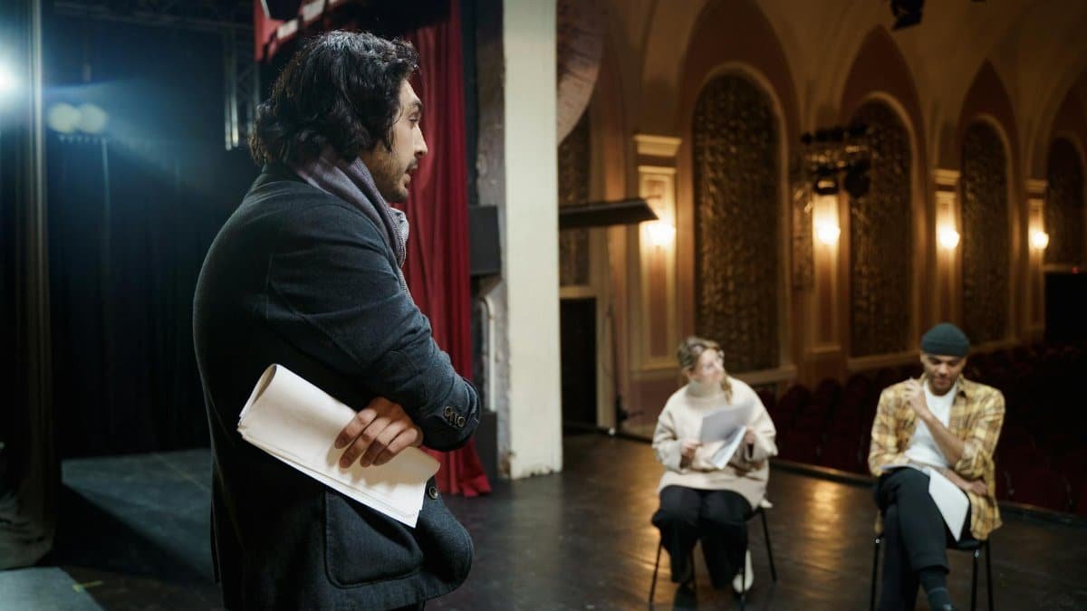 Actors rehearsing on stage in a vintage theater auditorium with a director observing.