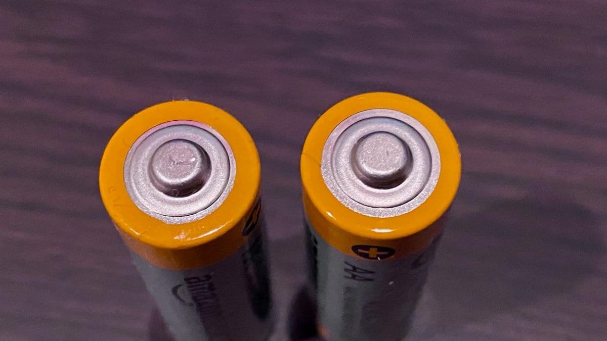 Top view of two AA batteries with yellow tops on a dark surface.