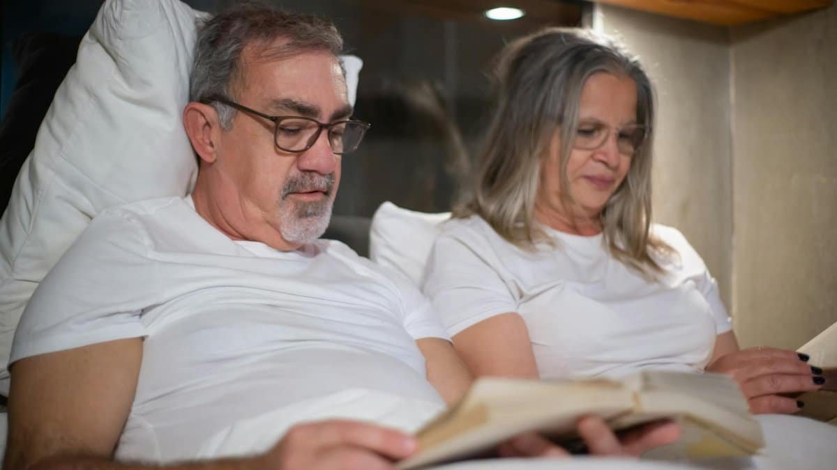 Senior couple enjoying leisure time reading in bed, fostering relaxation and connection.