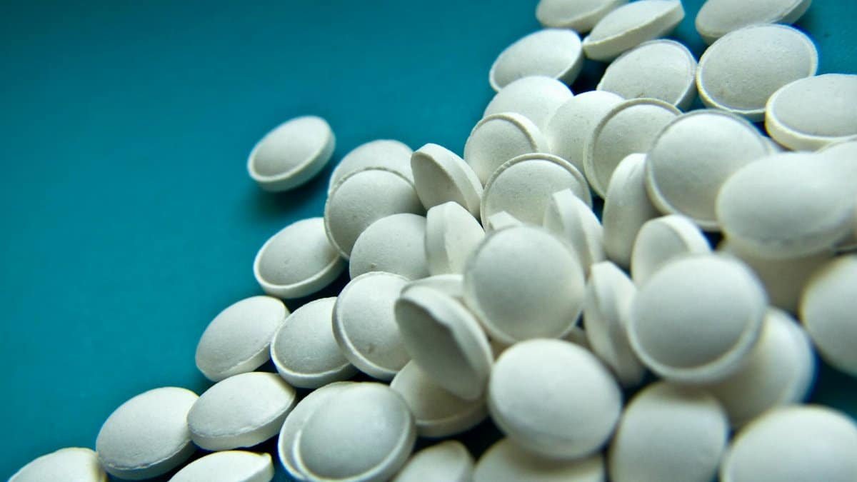 High angle of white round tablets for disease treatment scattered on blue background