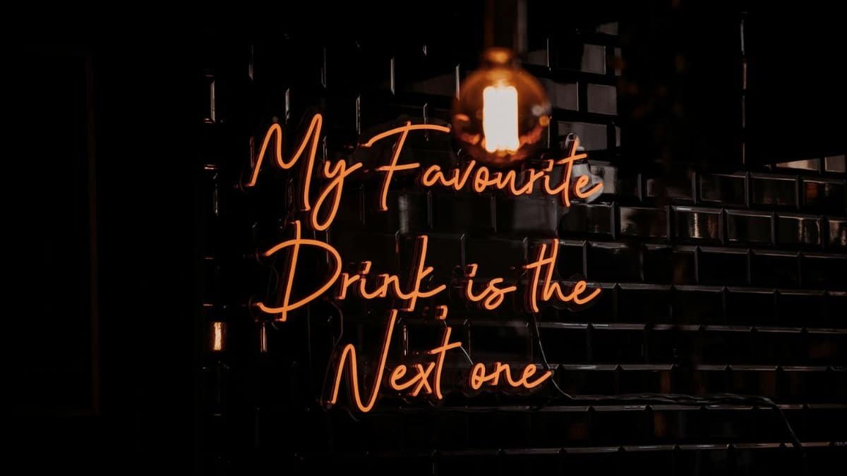 Moody shot of a neon bar sign reading 'My Favourite Drink is the Next One'.