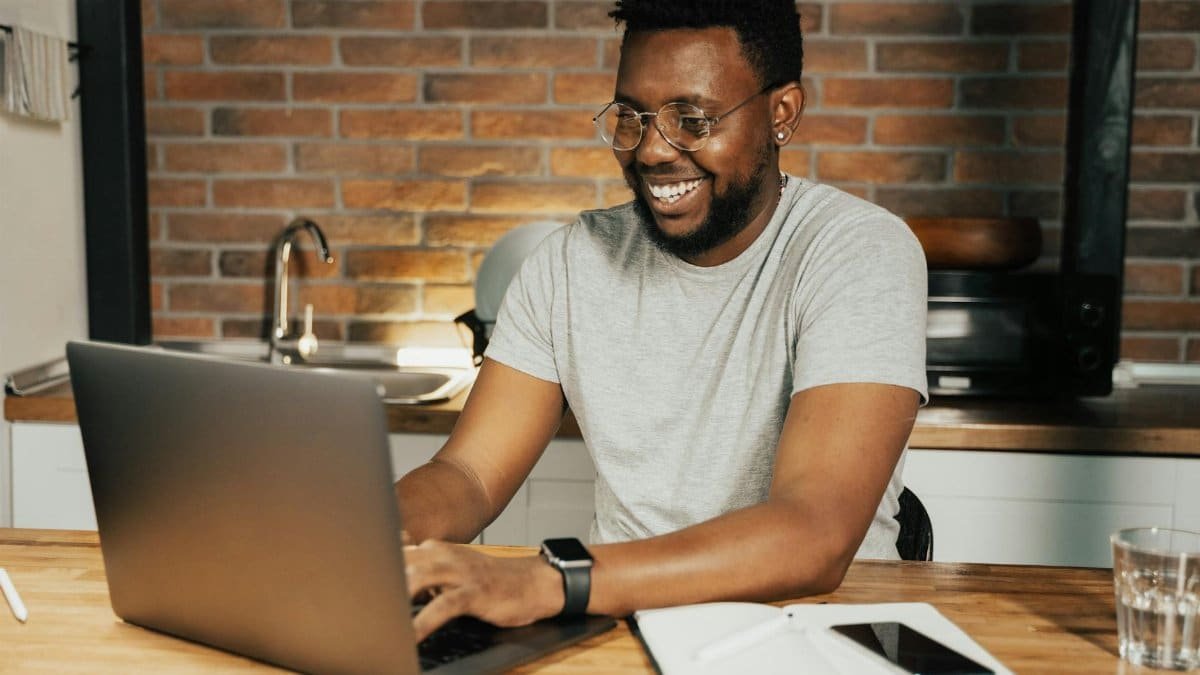 African American man smiling while working remotely on laptop from home office