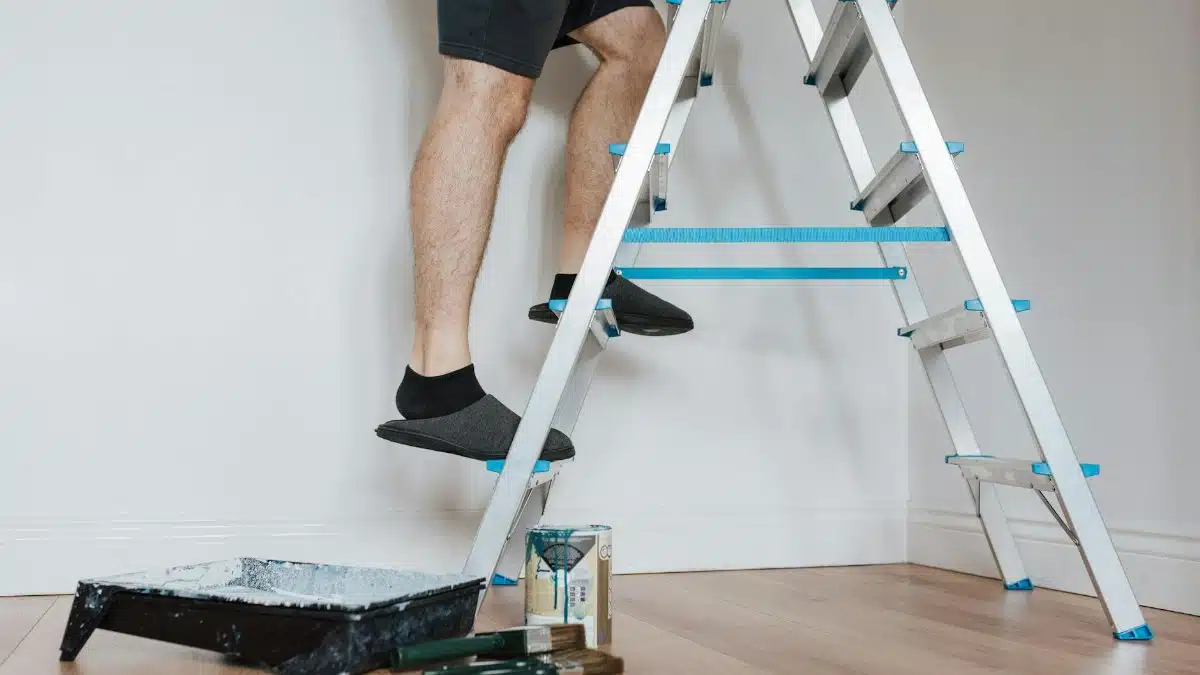 Side view of crop unrecognizable painter in slippers standing on stepladder while renovating room with brush in soft daylight