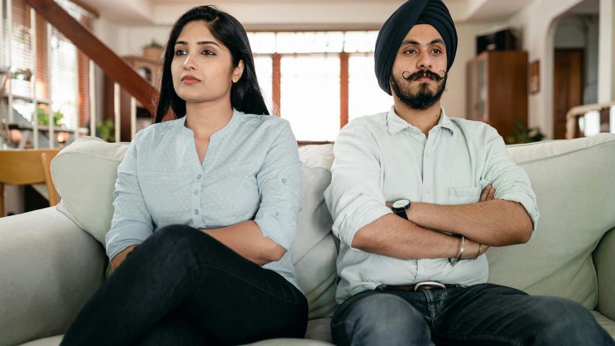 Resentful young Indian couple ignoring each other while sitting on couch together with crossed arms