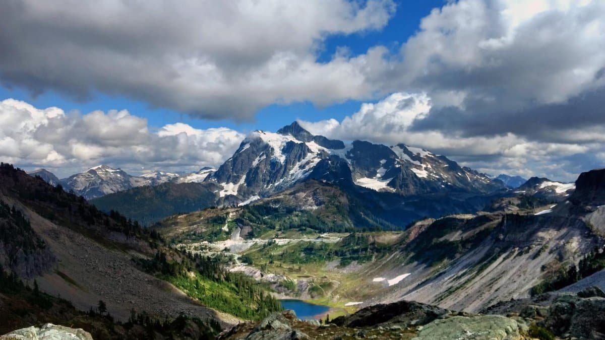 Stunning vista of Mount Shuksan with snow-capped peaks, lush valleys, and dramatic clouds.