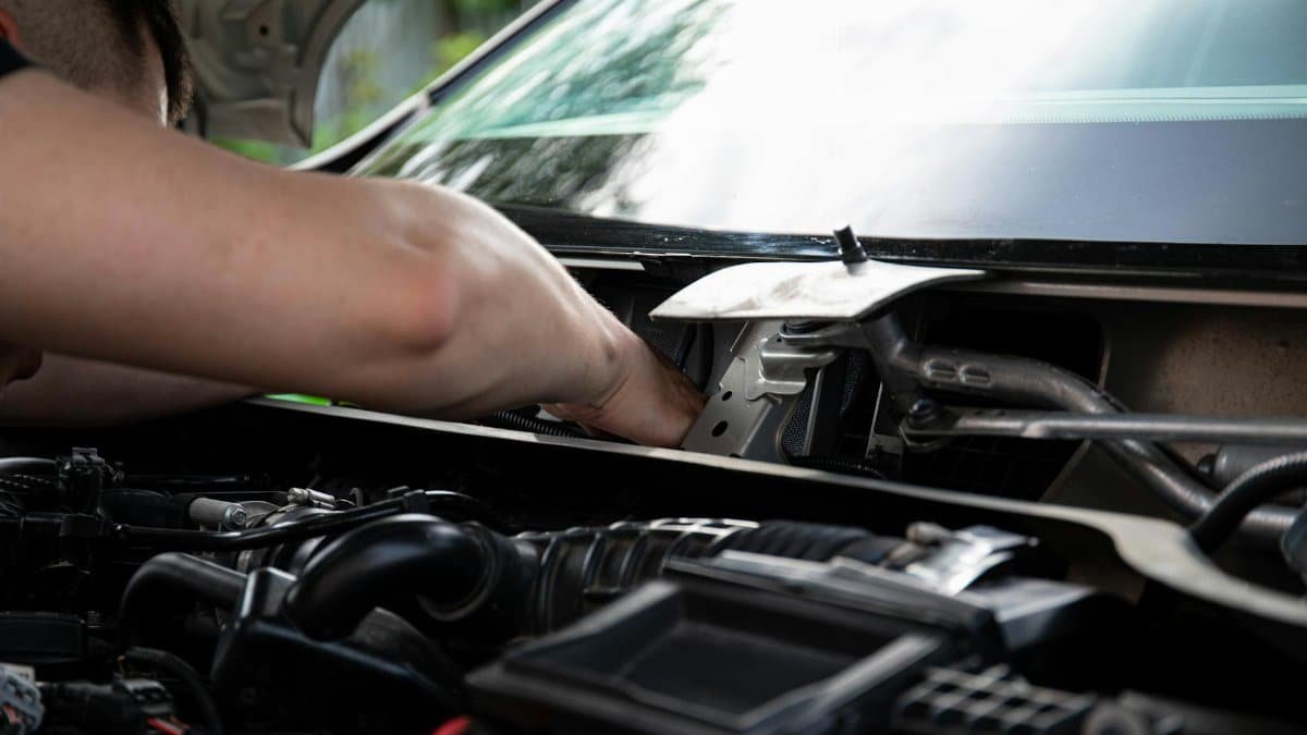 Mechanic performing engine maintenance on a car outdoors, focusing on repair work.