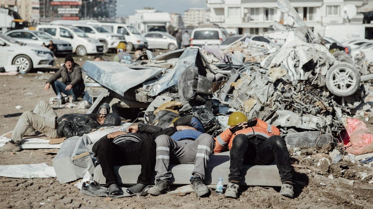 Rescuers rest on debris amidst a city after a disaster, showcasing urban ruins and resilience.